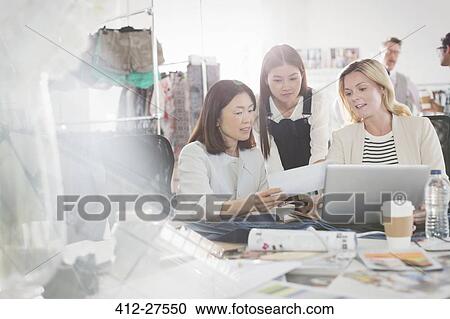Fashion designers discussing paperwork at laptop in office View Large Photo Image Stock Image - Fashion designers discussing paperwork at laptop in office. Fotosearch