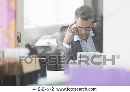 Focused businessman reviewing paperwork at desk in office View Large Photo Image Stock Image - Focused businessman reviewing paperwork at desk in office. Fotosearch