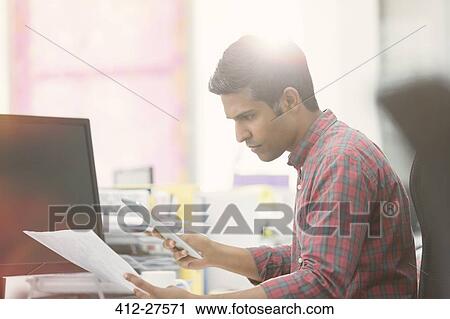 Focused businessman with digital tablet reviewing paperwork at desk in office View Large Photo Image Stock Image - Focused businessman with digital tablet reviewing paperwork at desk in office. Fotosearch
