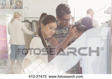 Stock Image - Photographer and fashion designer examining clothing. Fotosearch