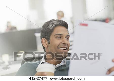 Smiling businessman drinking coffee and reviewing paperwork View Large Photo Image Stock Photo - Smiling businessman drinking coffee and reviewing paperwork. Fotosearch