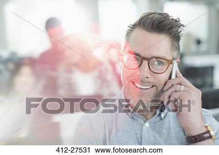 Stock Image - Smiling businessman talking on cell phone in office. Fotosearch