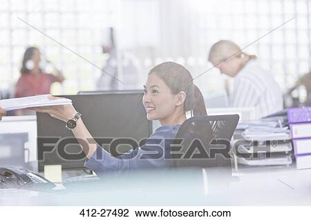 Smiling businesswoman holding paperwork at desk in office View Large Photo Image Stock Image - Smiling businesswoman holding paperwork at desk in office. Fotosearch