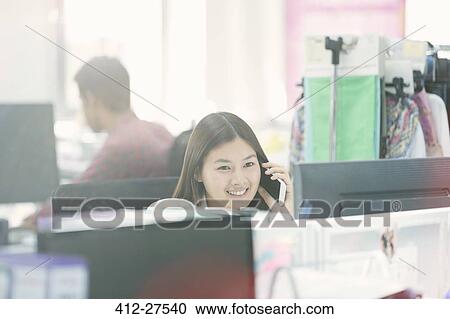 Smiling fashion designer talking on cell phone at desk in office View Large Photo Image Stock Image - Smiling fashion designer talking on cell phone at desk in office. Fotosearch