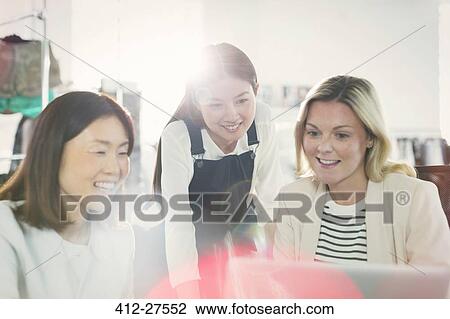 Smiling fashion designers working at laptop in office View Large Photo Image Stock Image - Smiling fashion designers working at laptop in office. Fotosearch