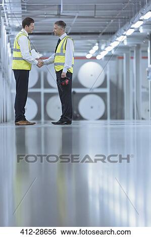 Businessmen in reflective clothing shaking hands in printing plant View Large Photo Image Stock Photograph - Businessmen in reflective clothing shaking hands in printing plant. Fotosearch