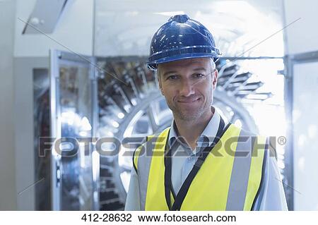 Stock Image - Portrait confident worker in reflective clothing and hard-hat in factory. Fotosearch