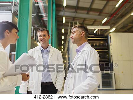 Stock Image - Scientists and businesswoman talking in factory. Fotosearch