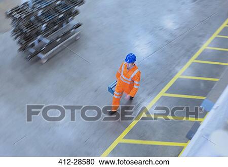 Stock Image - Worker in reflective clothing walking with toolbox in factory. Fotosearch