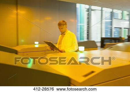 Stock Photograph - Worker with clipboard walking along printers in printing plant. Fotosearch