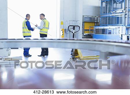 Stock Image - Workers in reflective clothing talking at warehouse loading dock doorway. Fotosearch
