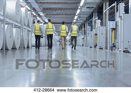 Workers in reflective clothing walking past large paper spools in printing plant View Large Photo Image Picture - Workers in reflective clothing walking past large paper spools in printing plant. Fotosearch