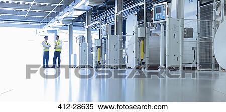 Workers talking along machinery in factory View Large Photo Image Stock Photography - Workers talking along machinery in factory. Fotosearch