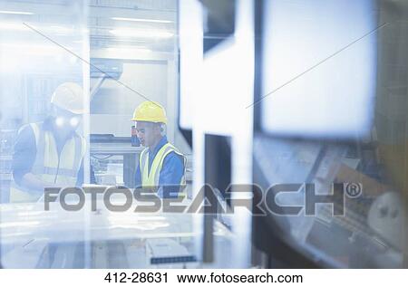 Stock Image - Workers talking at machinery in factory. Fotosearch