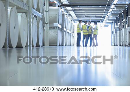Stock Image - Workers talking near large paper spools in printing plant. Fotosearch