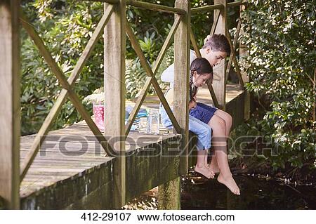 Brother and sister dangling bare feet over edge of footbridge View Large Photo Image Stock Photo - Brother and sister dangling bare feet over edge of footbridge. Fotosearch