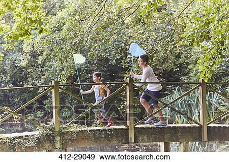 Brother and sister running with butterfly nets on footbridge in park View Large Photo Image Stock Photo - Brother and sister running with butterfly nets on footbridge in park. Fotosearch