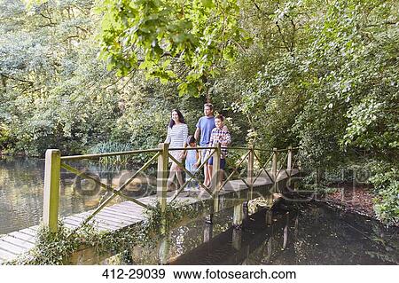 Family crossing footbridge in park with trees View Large Photo Image Stock Photo - Family crossing footbridge in park with trees. Fotosearch