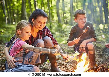 Stock Photography - Family roasting marshmallows at campfire in forest. Fotosearch