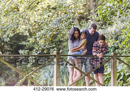 Family standing on footbridge in park with trees View Large Photo Image Stock Photograph - Family standing on footbridge in park with trees. Fotosearch