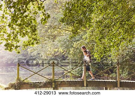 Stock Image - Father and son crossing footbridge in park with trees. Fotosearch