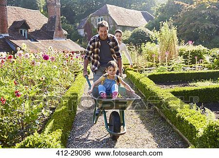 Father pushing daughter in wheelbarrow in sunny garden View Large Photo Image Stock Photograph - Father pushing daughter in wheelbarrow in sunny garden. Fotosearch