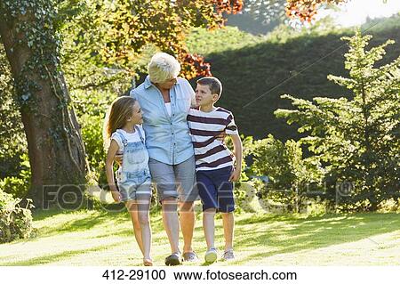 Stock Image - Grandmother and grandchildren walking in sunny garden. Fotosearch