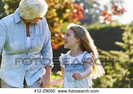 Grandmother and granddaughter holding hands and walking in sunny garden View Large Photo Image Stock Image - Grandmother and granddaughter holding hands and walking in sunny garden. Fotosearch