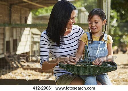 Stock Image - Mother and daughter with basket of eggs outside chicken coop. Fotosearch