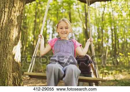 Stock Photography - Portrait smiling girl swinging on rope swing in forest. Fotosearch