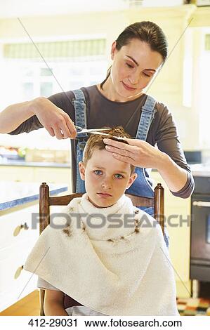 Stock Image - Portrait unhappy boy getting haircut from mother in kitchen. Fotosearch