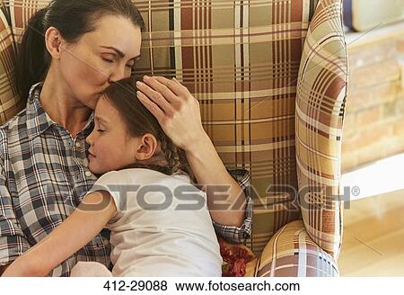 Stock Photo - Tender mother cuddling sleeping daughter in armchair. Fotosearch