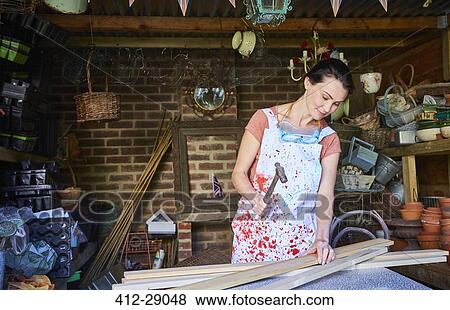 Stock Photo - Woman hammering wood boards in workshop. Fotosearch