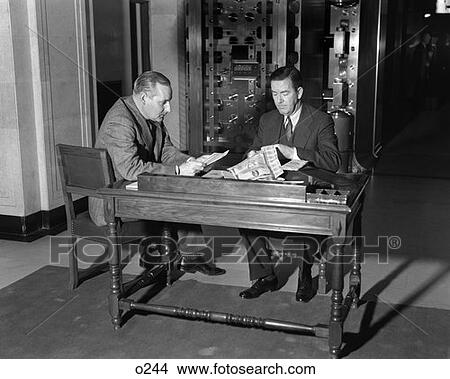 1930 1930S Two Men Seated At Table Before Bank Vault Safe Deposit Box Clipping Coupons Finance Security Retro View Large Photo Image Picture - 1930 1930S Two Men Seated At Table Before Bank Vault Safe Deposit Box Clipping Coupons Finance Security Retro. Fotosearch