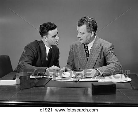 1940S 1950S Two Men Seated Desk Looking Over Business Papers View Large Photo Image Stock Image - 1940S 1950S Two Men Seated Desk Looking Over Business Papers . Fotosearch