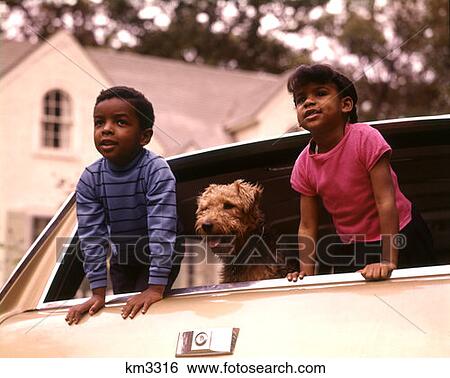 Stock Photograph - 1970 1970S African-American Children Boy Girl Pet Dog Looking Out Back Window Station Wagon Family Car . Fotosearch