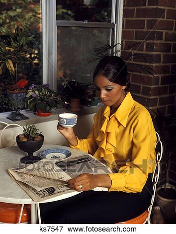 1970 1970S African-American Woman Yellow Blouse Sitting Table By Window Drinking Morning Coffee Reading Newspaper View Large Photo Image Stock Photo - 1970 1970S African-American Woman Yellow Blouse Sitting Table By Window Drinking Morning Coffee Reading Newspaper . Fotosearch