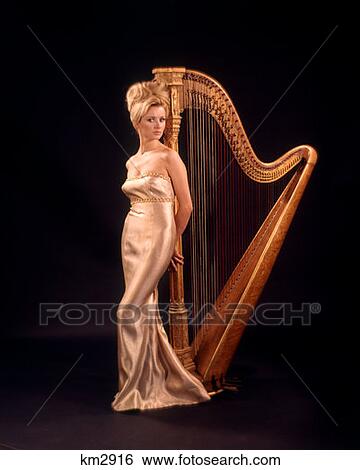 1970 1970S Blond Woman Gold Lame Long Gown Strapless Standing Front Harp Harps Black Background Women Harpist Musician View Large Photo Image Stock Photograph - 1970 1970S Blond Woman Gold Lame Long Gown Strapless Standing Front Harp Harps Black Background Women Harpist Musician . Fotosearch