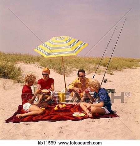 1970 1970S Family Beach Shore Picnic Eating Smiling Umbrella Fishing Poles Retro View Large Photo Image Stock Photo - 1970 1970S Family Beach Shore Picnic Eating Smiling Umbrella Fishing Poles Retro . Fotosearch