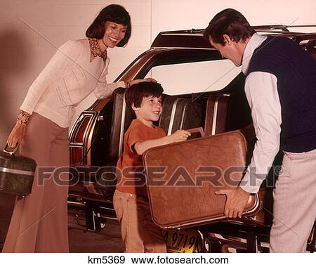 Stock Photo - 1970 1970S Family Loading Trunk Station Wagon For Road Trip Boy Son Hands Suitcase To Father Dad Man Woman Mother . Fotosearch