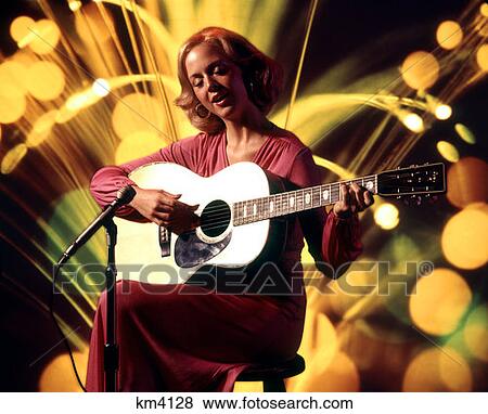1970 1970S Female Vocalist Woman Singing Playing Guitar Sitting Stool Microphone Acoustic Folk Singer Pink Dress View Large Photo Image Stock Photo - 1970 1970S Female Vocalist Woman Singing Playing Guitar Sitting Stool Microphone Acoustic Folk Singer Pink Dress . Fotosearch