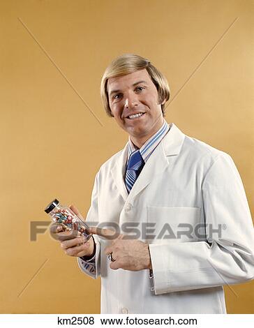 1970 1970S Man Doctor Pharmacist White Jacket Holding Bottle Pills Drug Drugs  View Large Photo Image Stock Photo - 1970 1970S Man Doctor Pharmacist White Jacket Holding Bottle Pills Drug Drugs . Fotosearch