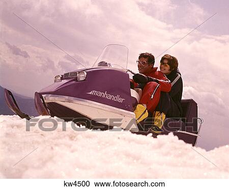 Stock Image - 1970 1970S Man Woman Couple Snowmobile Winter Sport Men Women Couples Snow Vehicle Skidoo Retro . Fotosearch