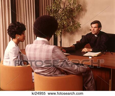 1970 1970S Priest Minister Clergy Man Interviewing Consulting African-American Couple Man Woman Desk Office Religion View Large Photo Image Stock Photography - 1970 1970S Priest Minister Clergy Man Interviewing Consulting African-American Couple Man Woman Desk Office Religion . Fotosearch