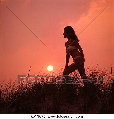 Stock Photography - 1970 1970S Silhouette Silhouetted Woman Atop Sand Dune Sunset Mood Moody Sunsets Beach Dunes Vacaton Alone Single Retro . Fotosearch