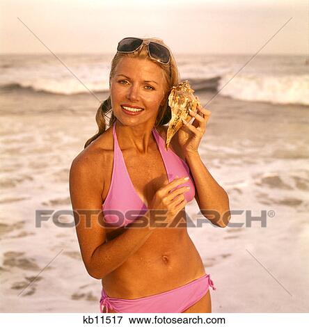 1970 1970S Smiling Sexy Woman Lavender Bikini Beach Surf Holding Seashell To Ear Listen Listening Ocean Hear Retro View Large Photo Image Stock Photo - 1970 1970S Smiling Sexy Woman Lavender Bikini Beach Surf Holding Seashell To Ear Listen Listening Ocean Hear Retro . Fotosearch