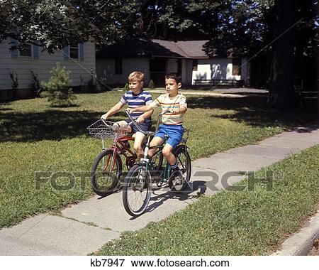 1970 1970S Two Boys Riding Bikes Biking Down Suburban Neighborhood Sidewalk View Large Photo Image Stock Photo - 1970 1970S Two Boys Riding Bikes Biking Down Suburban Neighborhood Sidewalk . Fotosearch