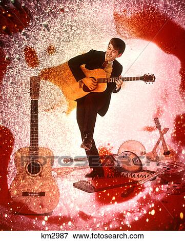 Stock Photo - 1970 1970S Young Man Musician Playing Guitar Rock Music Surrounded By Special Effects Guitars Colors Psychedelic . Fotosearch