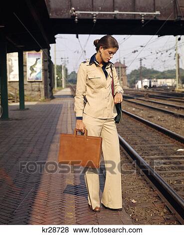 Stock Photo - 1970 1970S Young Woman Businesswoman On Train Platform Look At Watch Briefcase Commuter Commute Business Retro . Fotosearch