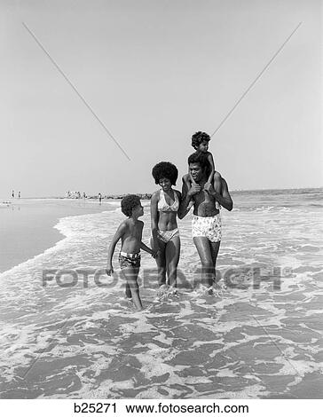 Stock Image - 1970S African-American Family Wading In Surf Walking Along Beach . Fotosearch